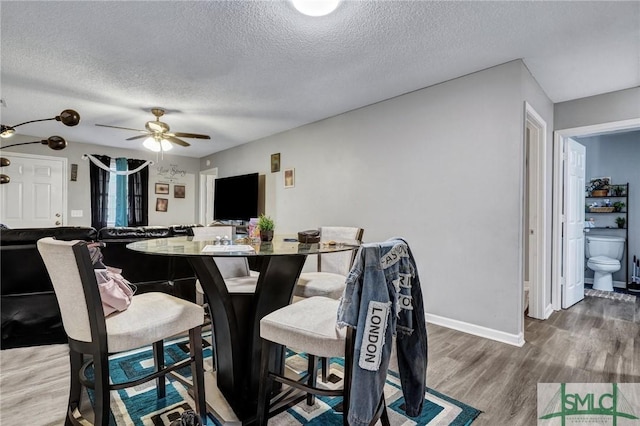 dining area with a ceiling fan, wood finished floors, baseboards, and a textured ceiling