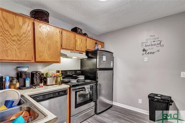 kitchen featuring wood finished floors, a sink, stainless steel appliances, under cabinet range hood, and a textured ceiling