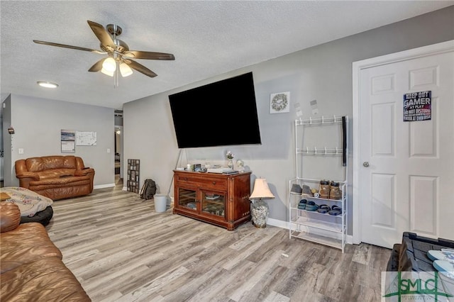 living room featuring baseboards, a textured ceiling, a ceiling fan, and wood finished floors