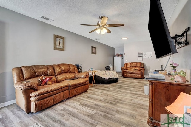 living room featuring light wood finished floors, visible vents, a textured ceiling, and a ceiling fan