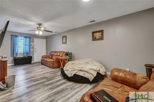 living room with visible vents, a ceiling fan, a textured ceiling, wood finished floors, and baseboards