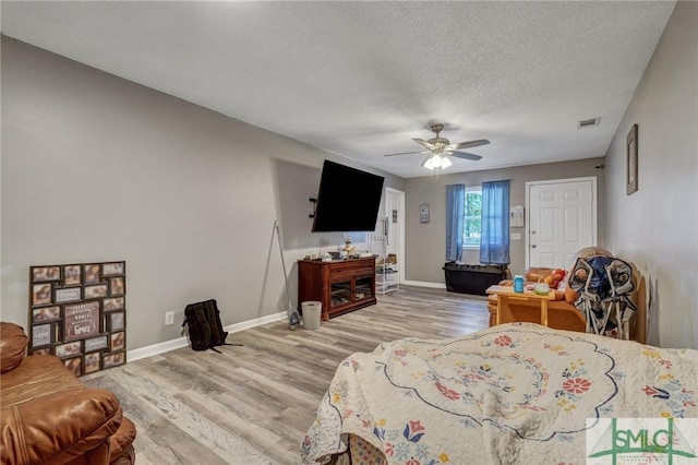 bedroom with a ceiling fan, light wood-style floors, baseboards, and a textured ceiling