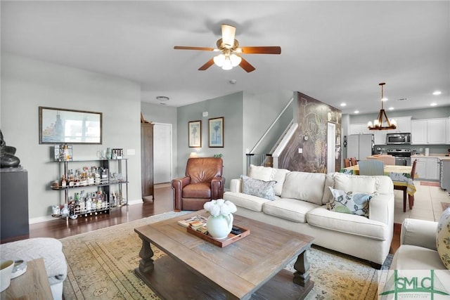 living room with recessed lighting, ceiling fan with notable chandelier, light wood-style floors, and baseboards