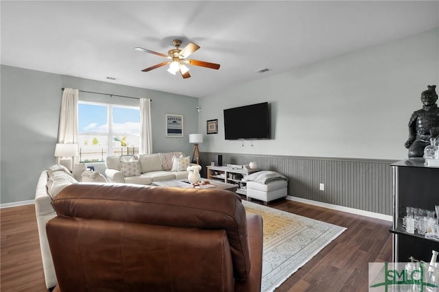 living area featuring visible vents, dark wood-type flooring, baseboards, a wainscoted wall, and a ceiling fan