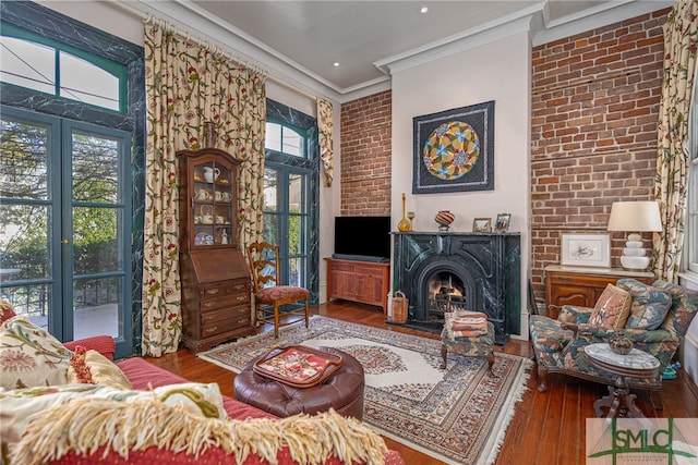 living area featuring wood-type flooring, plenty of natural light, a warm lit fireplace, and crown molding