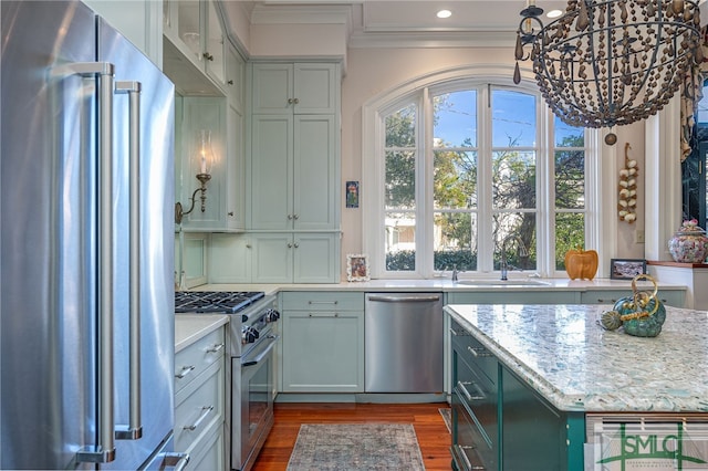 kitchen with dark wood finished floors, ornamental molding, light stone counters, high end appliances, and a sink