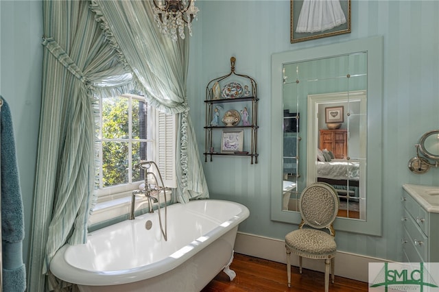 ensuite bathroom featuring connected bathroom, baseboards, a freestanding bath, wood finished floors, and vanity