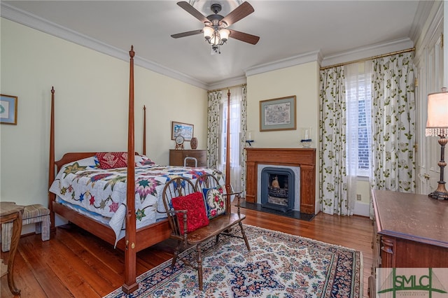 bedroom featuring a ceiling fan, a fireplace with flush hearth, wood finished floors, and ornamental molding