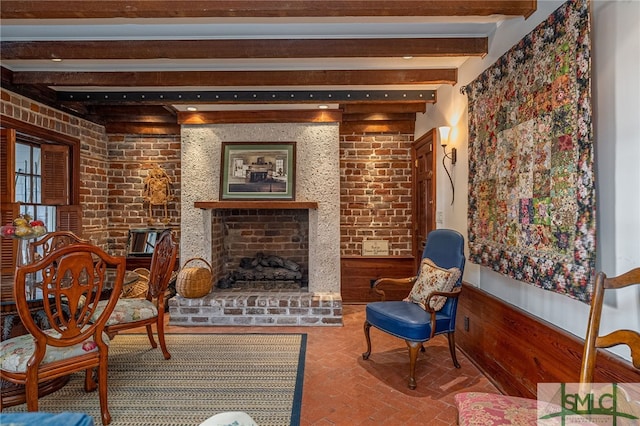 living area featuring a wainscoted wall, brick wall, a fireplace, brick floor, and beamed ceiling