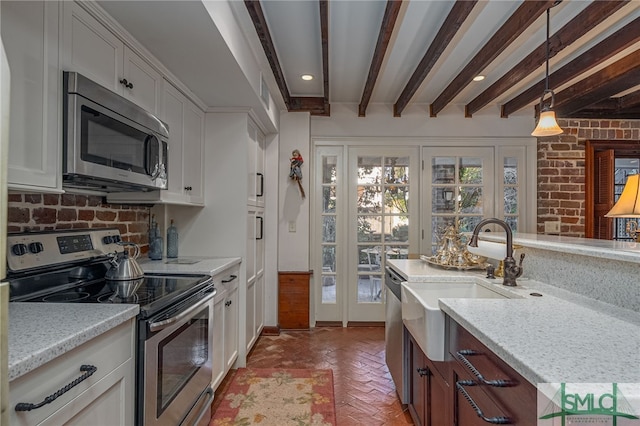 kitchen with beamed ceiling, pendant lighting, a sink, stainless steel appliances, and brick floor