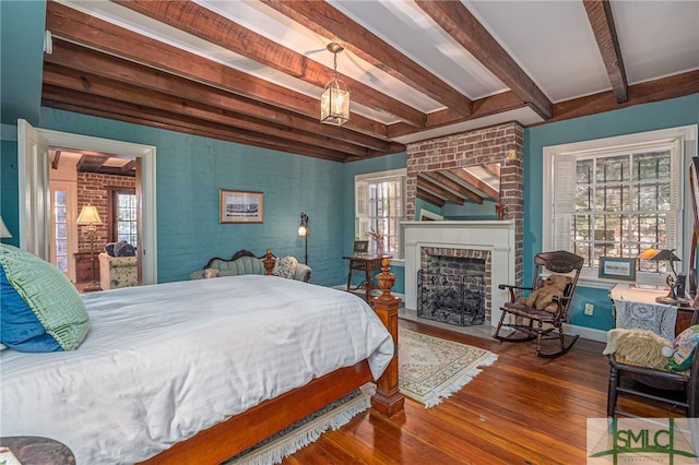 bedroom with beamed ceiling, wood finished floors, brick wall, baseboards, and a brick fireplace