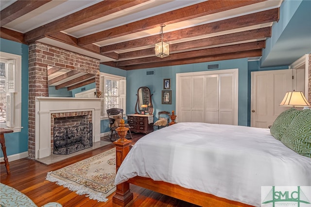 bedroom featuring a fireplace, beamed ceiling, wood finished floors, and visible vents