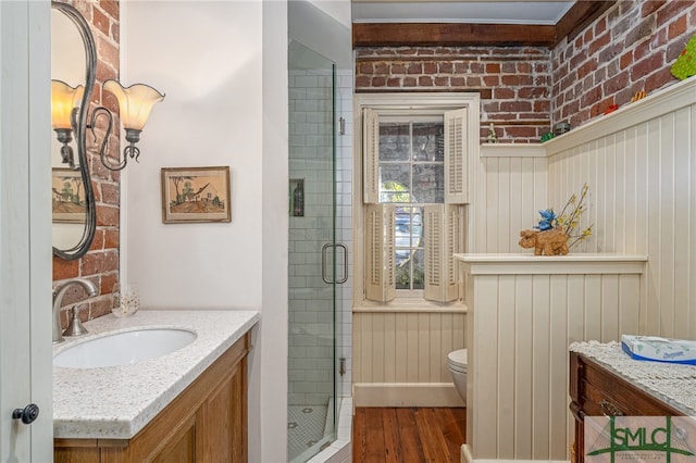 full bath with vanity, wood finished floors, brick wall, a stall shower, and toilet