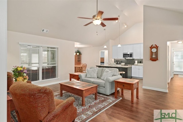 living room featuring visible vents, baseboards, wood finished floors, high vaulted ceiling, and a ceiling fan