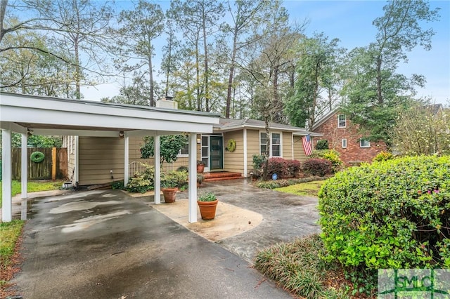 view of front of home featuring a carport, driveway, a chimney, and fence