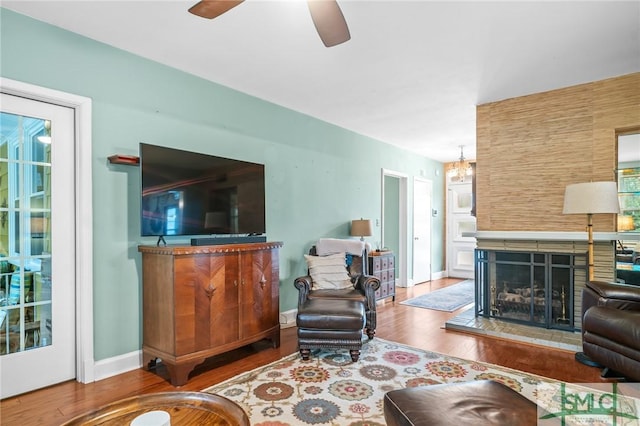 living area featuring baseboards, wood finished floors, a multi sided fireplace, and ceiling fan