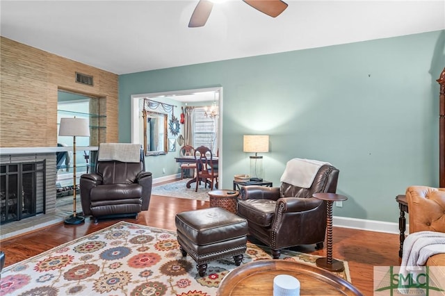 living area with visible vents, wood finished floors, baseboards, and a fireplace with raised hearth