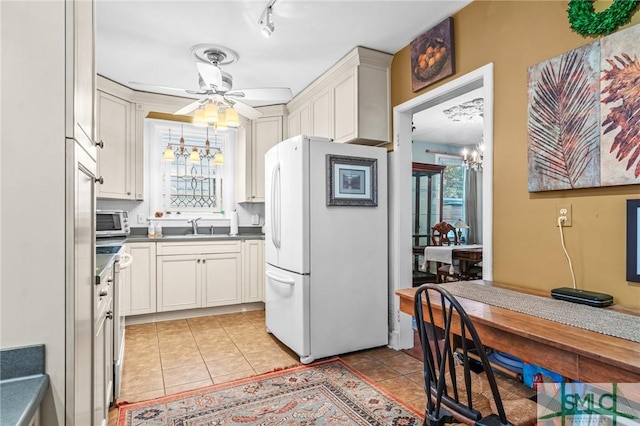 kitchen with stainless steel microwave, freestanding refrigerator, light tile patterned flooring, white cabinets, and a sink