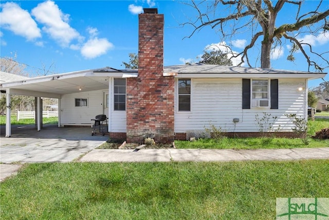 view of side of home featuring cooling unit, a chimney, concrete driveway, a carport, and a lawn