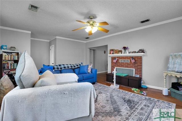 living area with visible vents, a brick fireplace, a textured ceiling, and wood finished floors