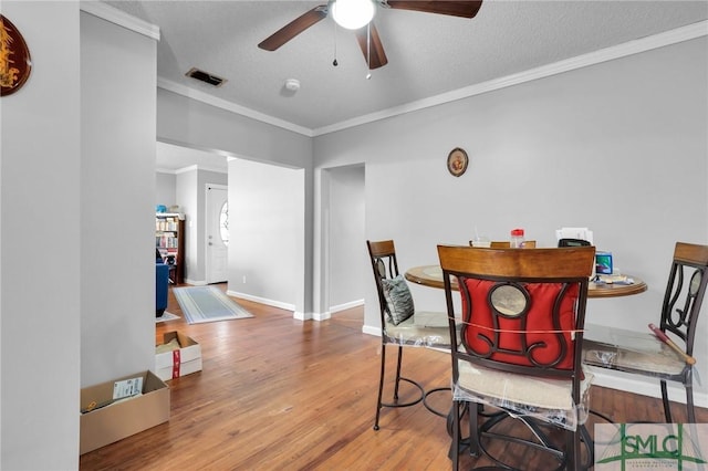 dining space featuring visible vents, crown molding, baseboards, wood finished floors, and a textured ceiling