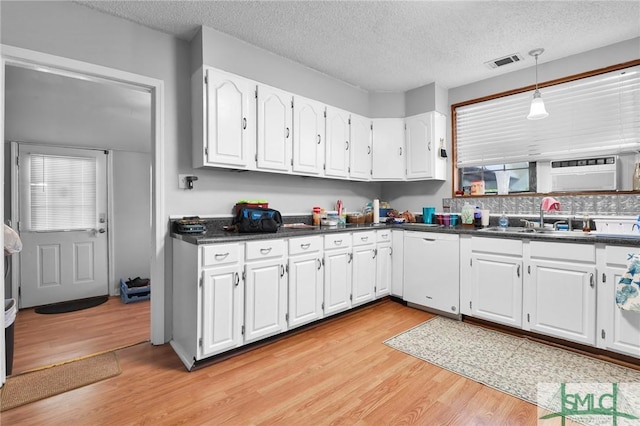 kitchen featuring visible vents, dark countertops, white cabinetry, light wood finished floors, and dishwasher