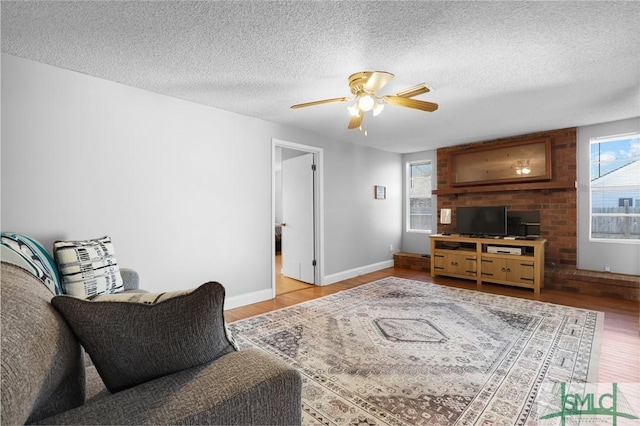 living area featuring baseboards, a textured ceiling, wood finished floors, and a ceiling fan