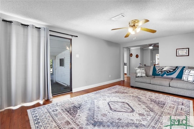 living room featuring visible vents, baseboards, a textured ceiling, and wood finished floors