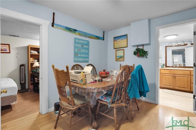 dining space with visible vents, a textured ceiling, light wood-type flooring, and baseboards