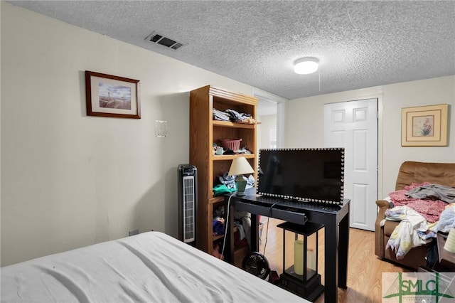 bedroom with light wood finished floors, visible vents, and a textured ceiling