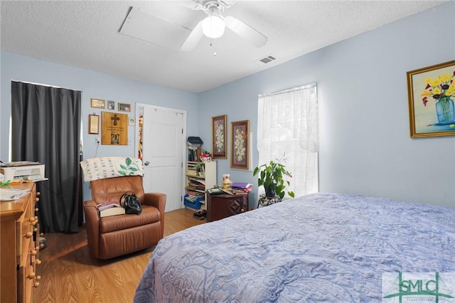 bedroom with a ceiling fan, wood finished floors, visible vents, and a textured ceiling