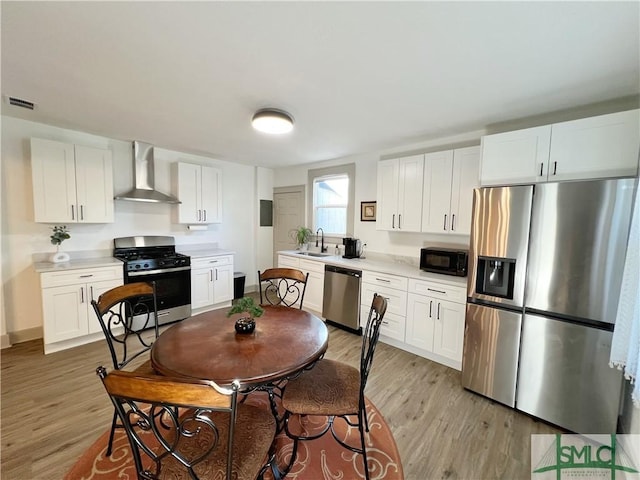 kitchen featuring visible vents, light wood finished floors, a sink, appliances with stainless steel finishes, and wall chimney exhaust hood