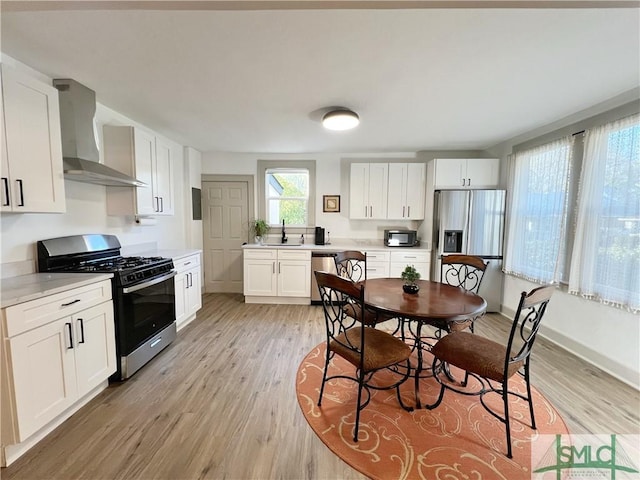 kitchen featuring light wood-style flooring, stainless steel appliances, wall chimney range hood, and a sink