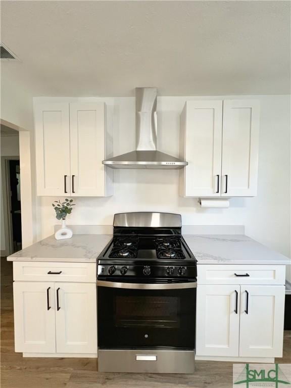 kitchen featuring visible vents, stainless steel gas stove, white cabinetry, wall chimney range hood, and light stone countertops