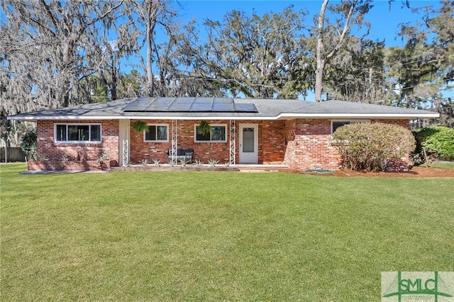 ranch-style house featuring brick siding, solar panels, a front lawn, and a patio area