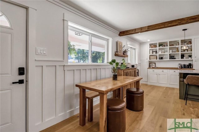 dining room with beam ceiling, a decorative wall, light wood-style flooring, and a wainscoted wall