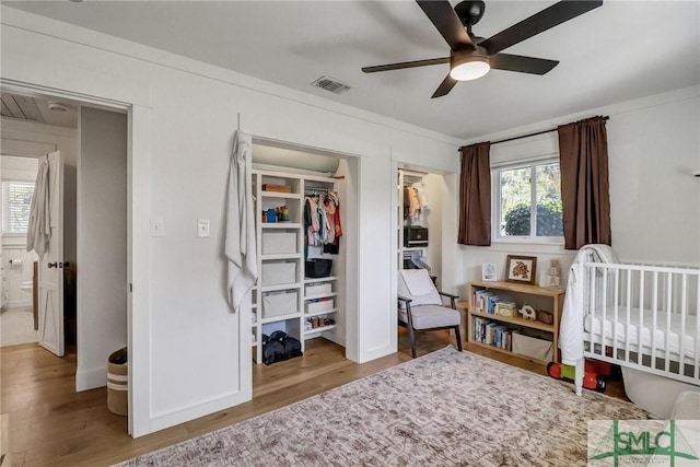 bedroom featuring ceiling fan, visible vents, multiple windows, and wood finished floors