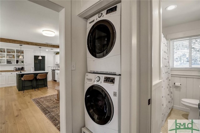 clothes washing area featuring stacked washer / drying machine, light wood-style floors, and laundry area