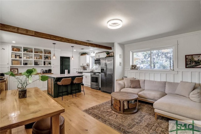 living room with beamed ceiling, visible vents, a wainscoted wall, and light wood finished floors