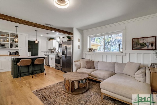 living area with visible vents, beamed ceiling, and light wood-style floors