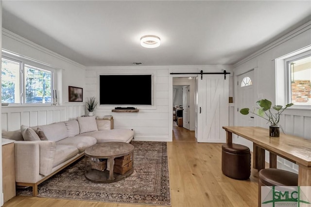 living room featuring a barn door, light wood-style flooring, visible vents, and ornamental molding