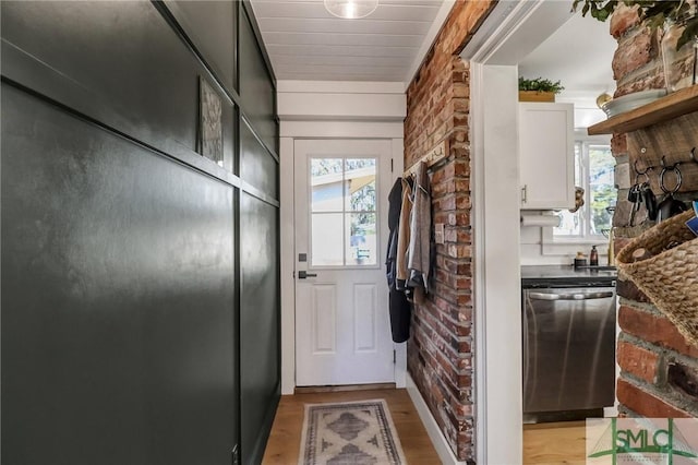 doorway to outside with brick wall, light wood-type flooring, and a wealth of natural light