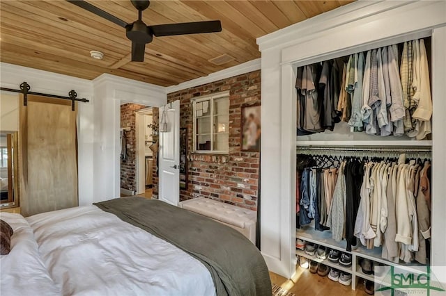 bedroom featuring a barn door, wooden ceiling, a closet, and brick wall