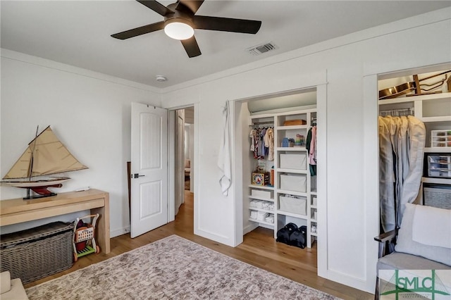 bedroom featuring visible vents, crown molding, baseboards, wood finished floors, and a ceiling fan