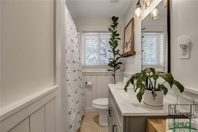 bathroom featuring a shower with shower curtain, wainscoting, toilet, and vanity