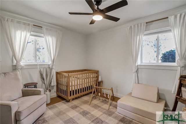 bedroom with a crib, multiple windows, baseboards, and ceiling fan