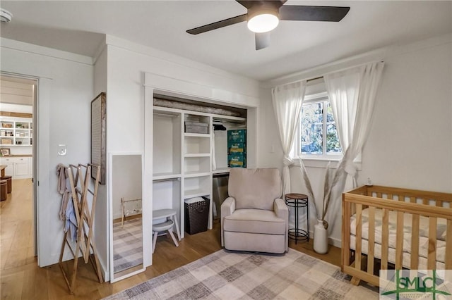 bedroom featuring a closet, a nursery area, light wood-type flooring, and ceiling fan