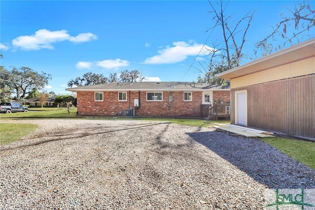 back of property featuring gravel driveway, a yard, central AC, a garage, and brick siding