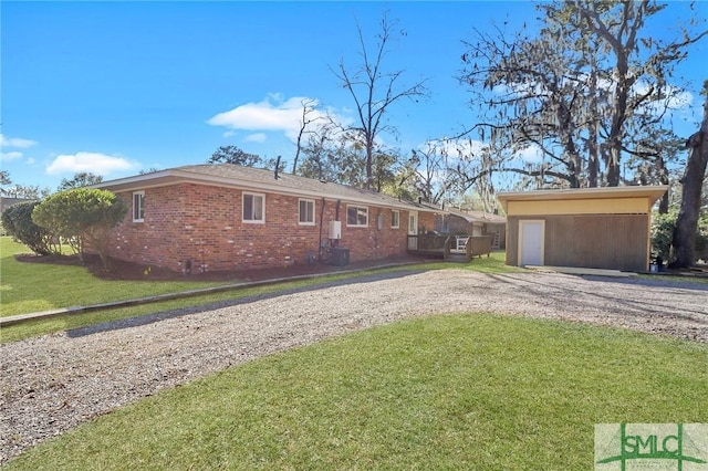 exterior space featuring an outbuilding, brick siding, gravel driveway, and a front yard