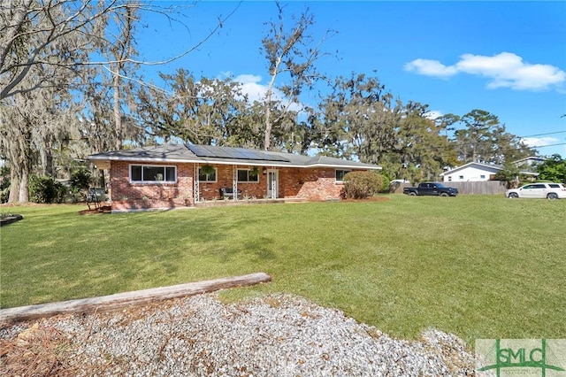 ranch-style house with a front lawn, roof mounted solar panels, a porch, fence, and brick siding